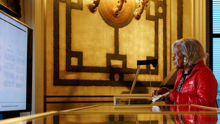 A woman in a red jacket looks at a large screen in a Reading Room at the Library of Congress.